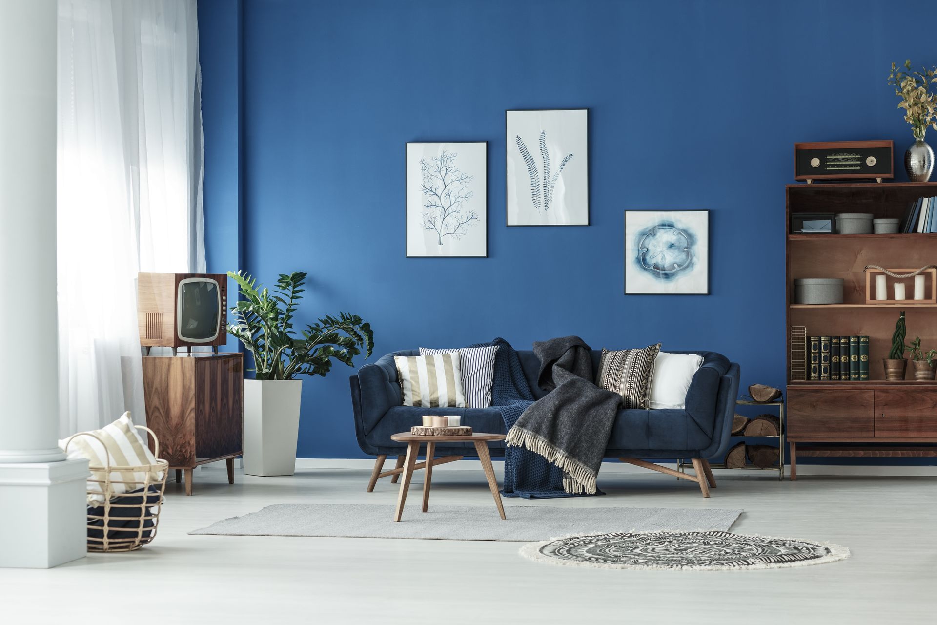 Salon bleu avec canapé foncé, tableaux encadrés et décoration moderne sur un sol clair.