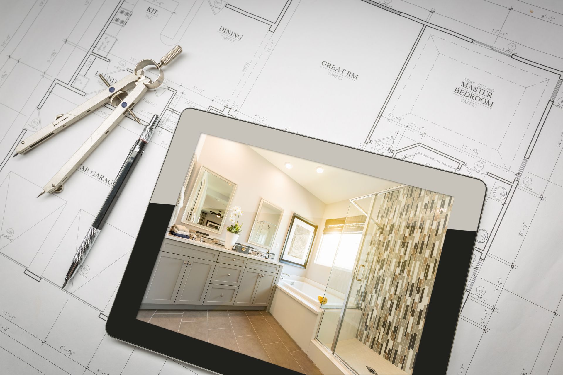 Tablette présentant un plan de salle de bains lumineux sur un plan d'architecte, avec des outils de dessin à côté.
