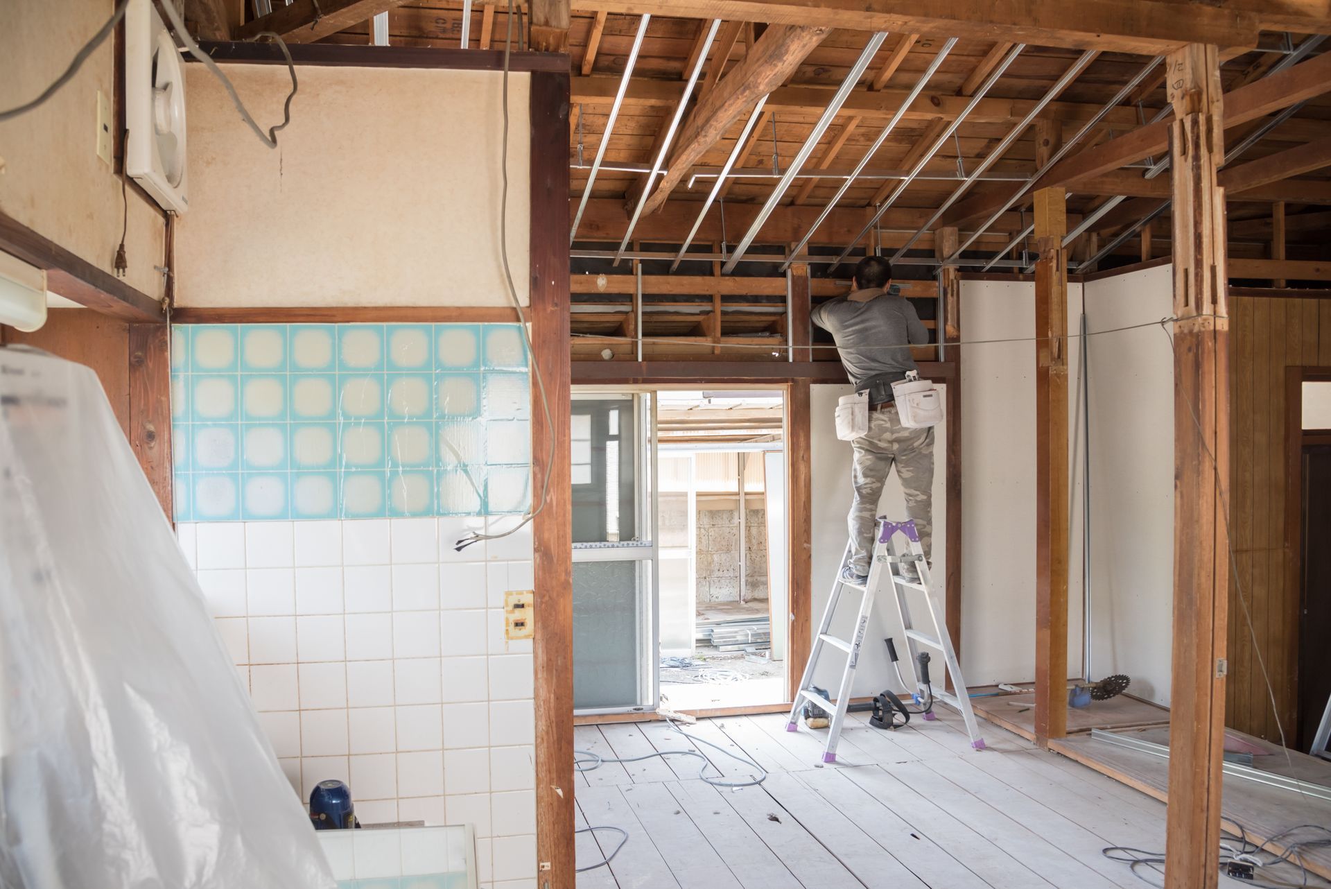 Intérieur en rénovation avec charpente apparente, mur carrelé et échelle dans une pièce partiellement démolie