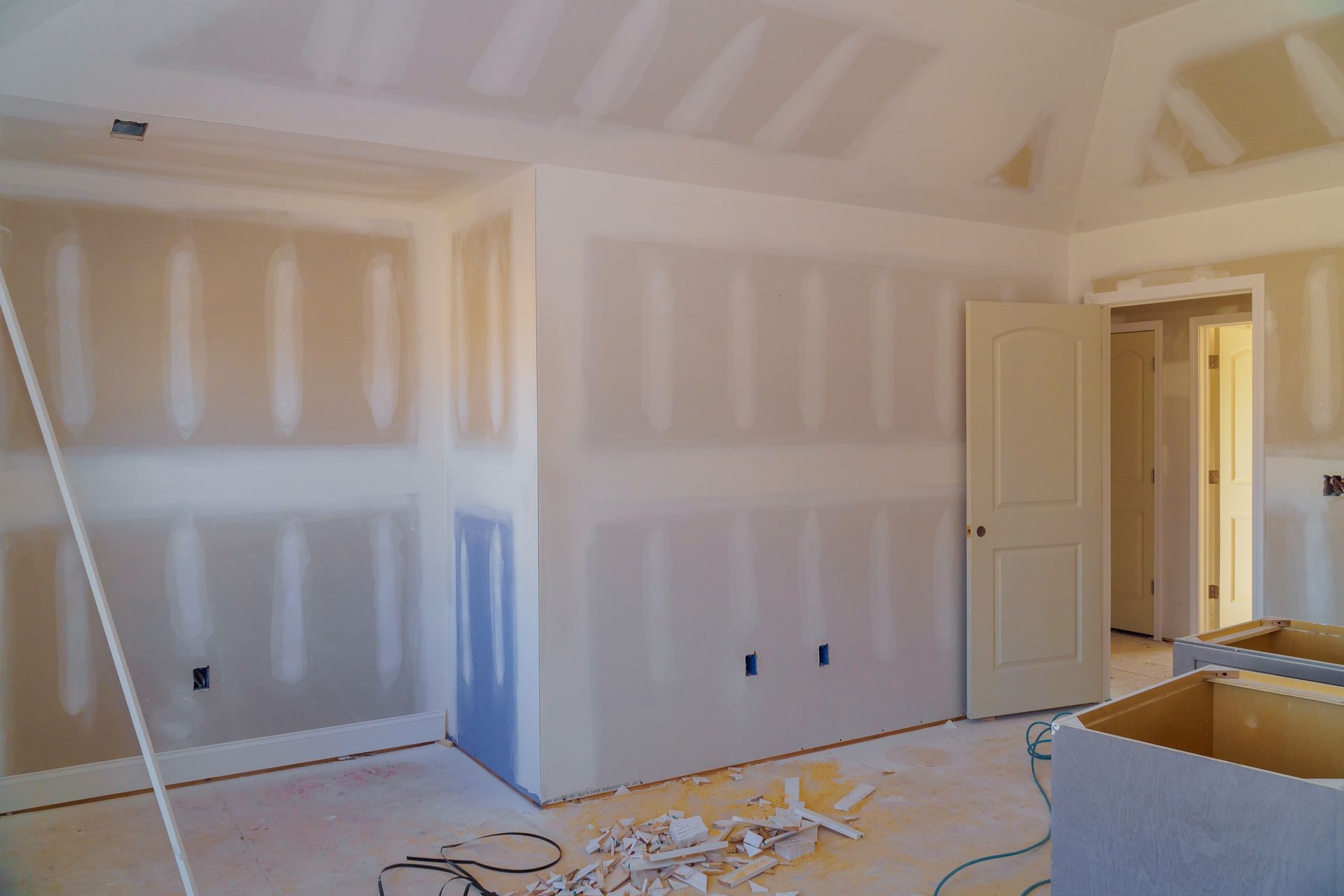 Pièce en rénovation, fraîchement cloisonnée, avec murs et plafond blancs, et portes ouvertes.