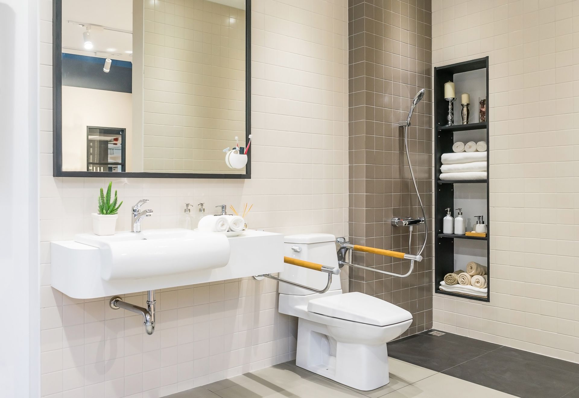 Salle de bains accessible avec lavabo, toilettes, barres d'appui et étagères ouvertes à côté d'un grand miroir.