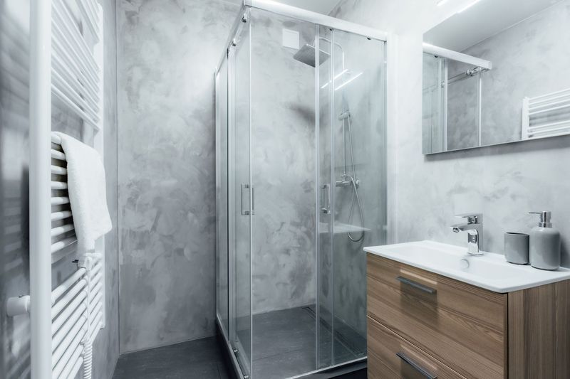 Salle de bains moderne avec douche en verre, lavabo blanc, meuble-lavabo en bois et murs carrelés gris.