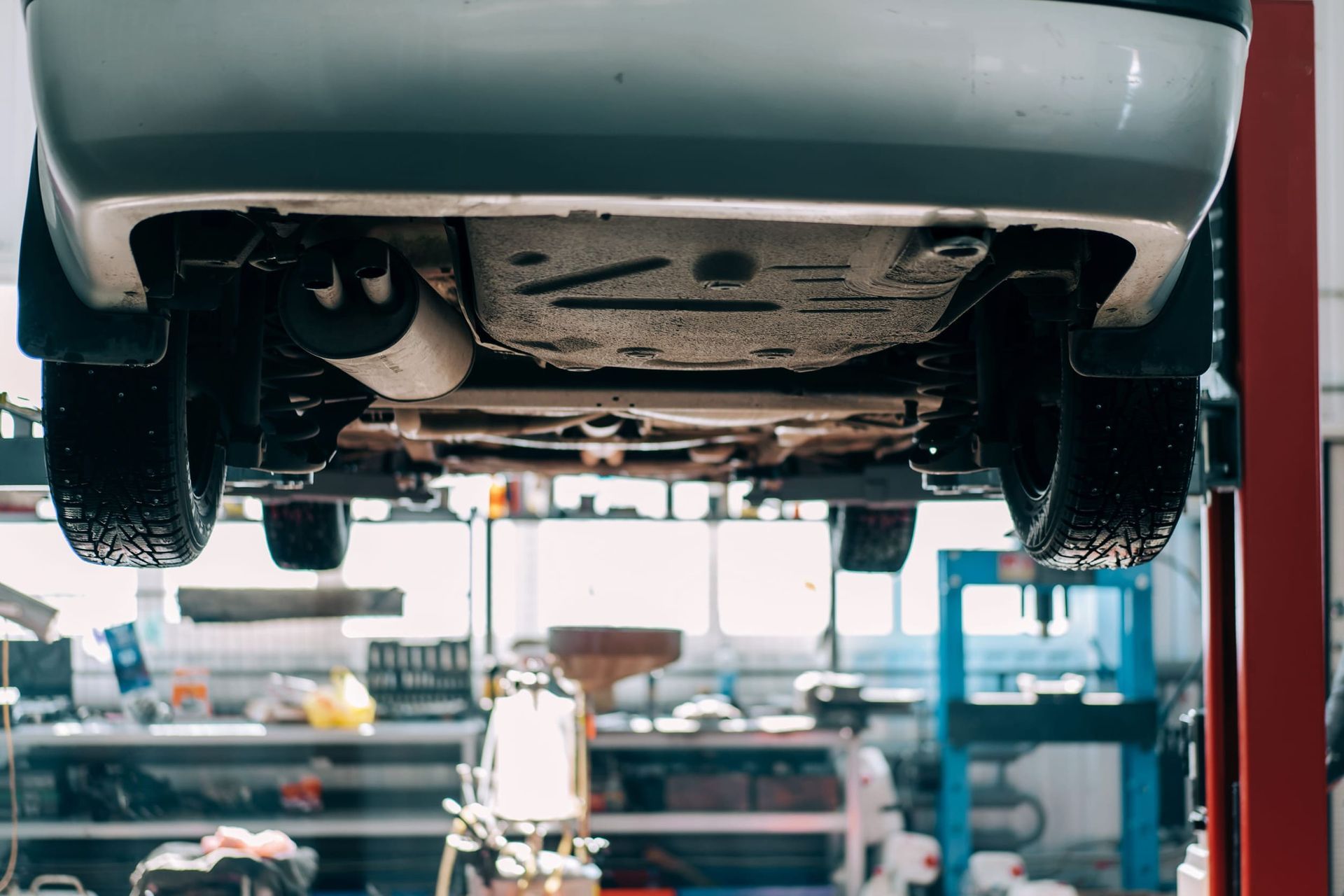 Dos mecánicos con uniformes azules trabajan en un coche plateado que está elevado en un taller de mantenimiento de automóviles luminoso y profesional.