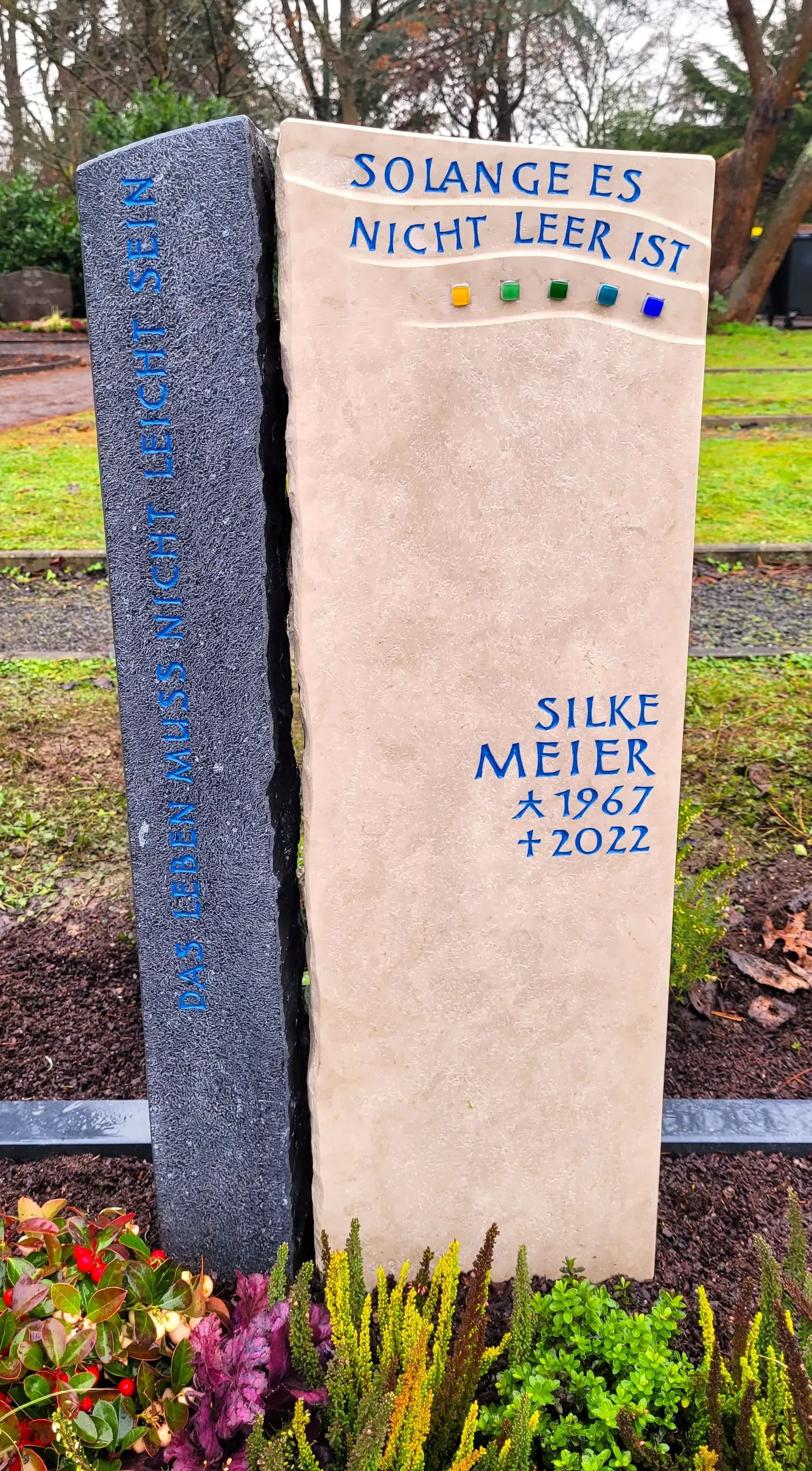 Zweiteiliger Gedenkstein mit blauer Inschrift und einer Reihe kleiner, bunter Glasquadrate.