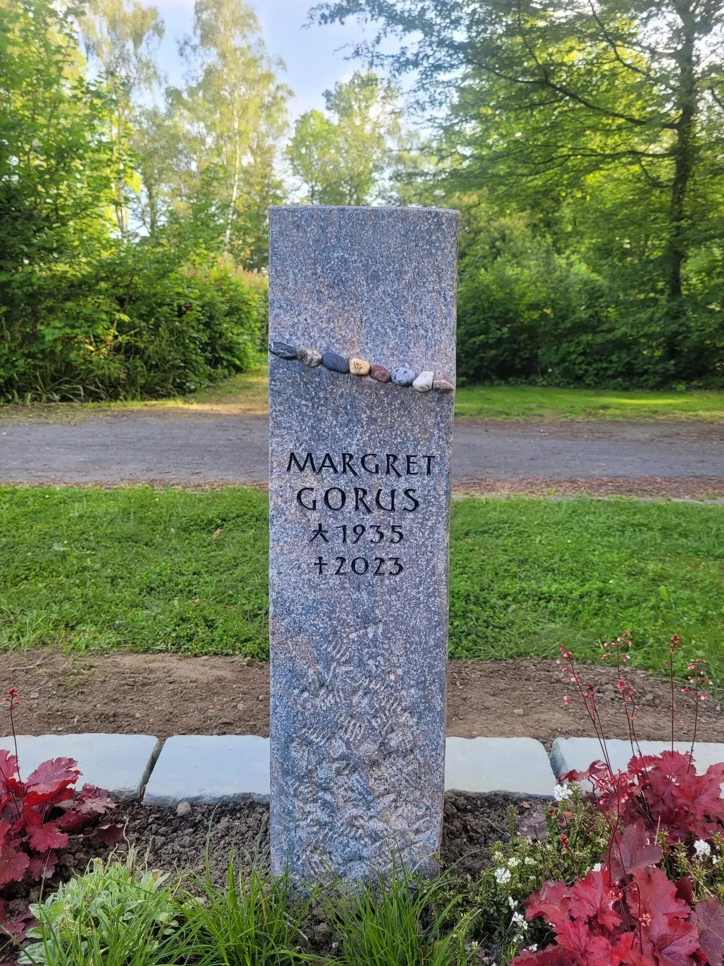 Hohe Stele aus grauem Naturstein mit einem Band aus bunten Kieseln.