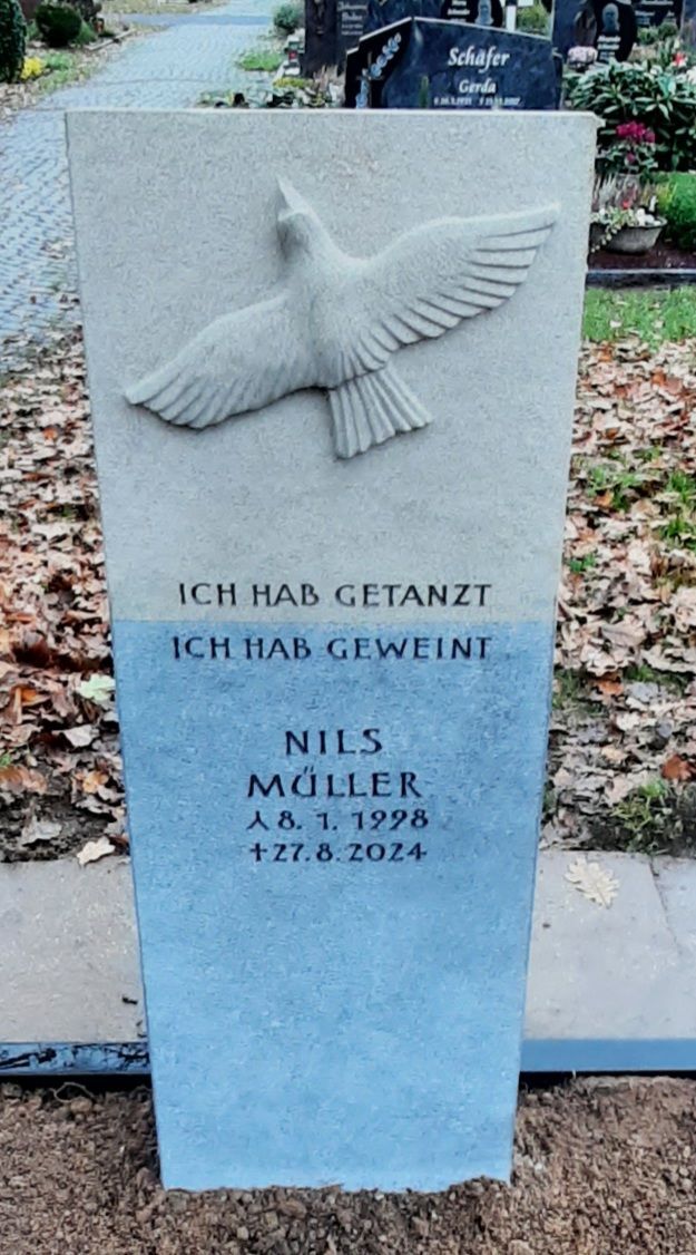 Grauer Gedenkstein mit Taubenrelief und deutscher Inschrift auf einem Friedhof