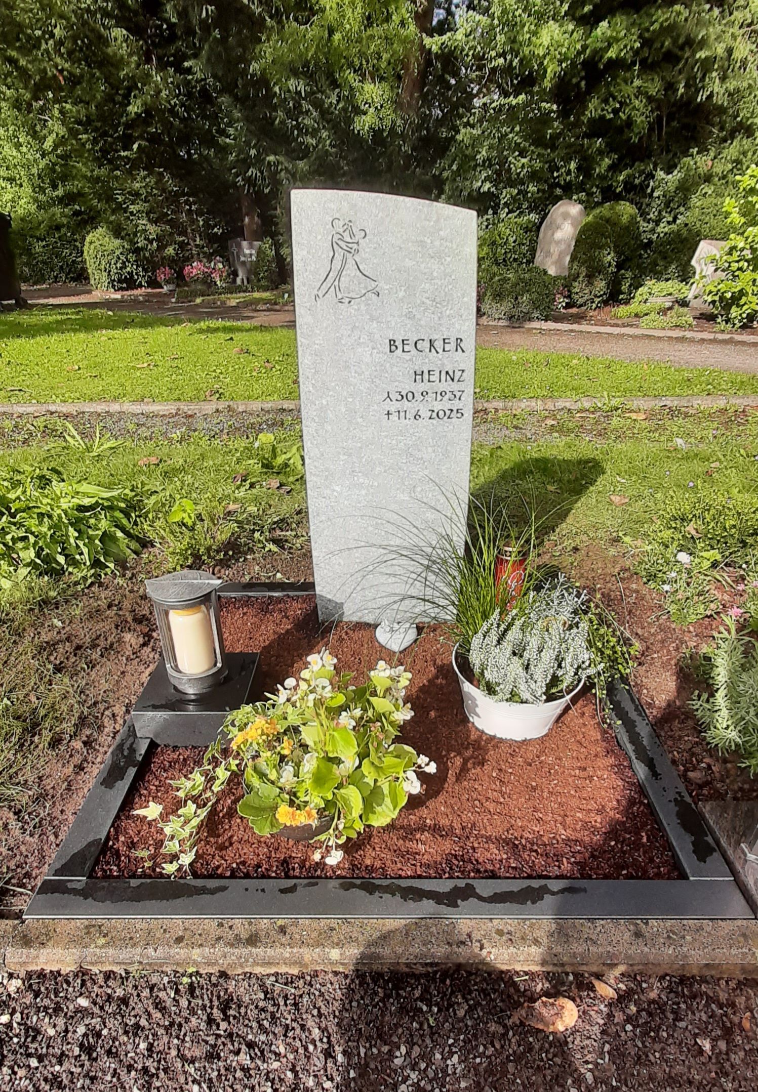 Geschmückter Grabstein auf einer gepflegten Grabstätte mit Blumen und einer Kerze
