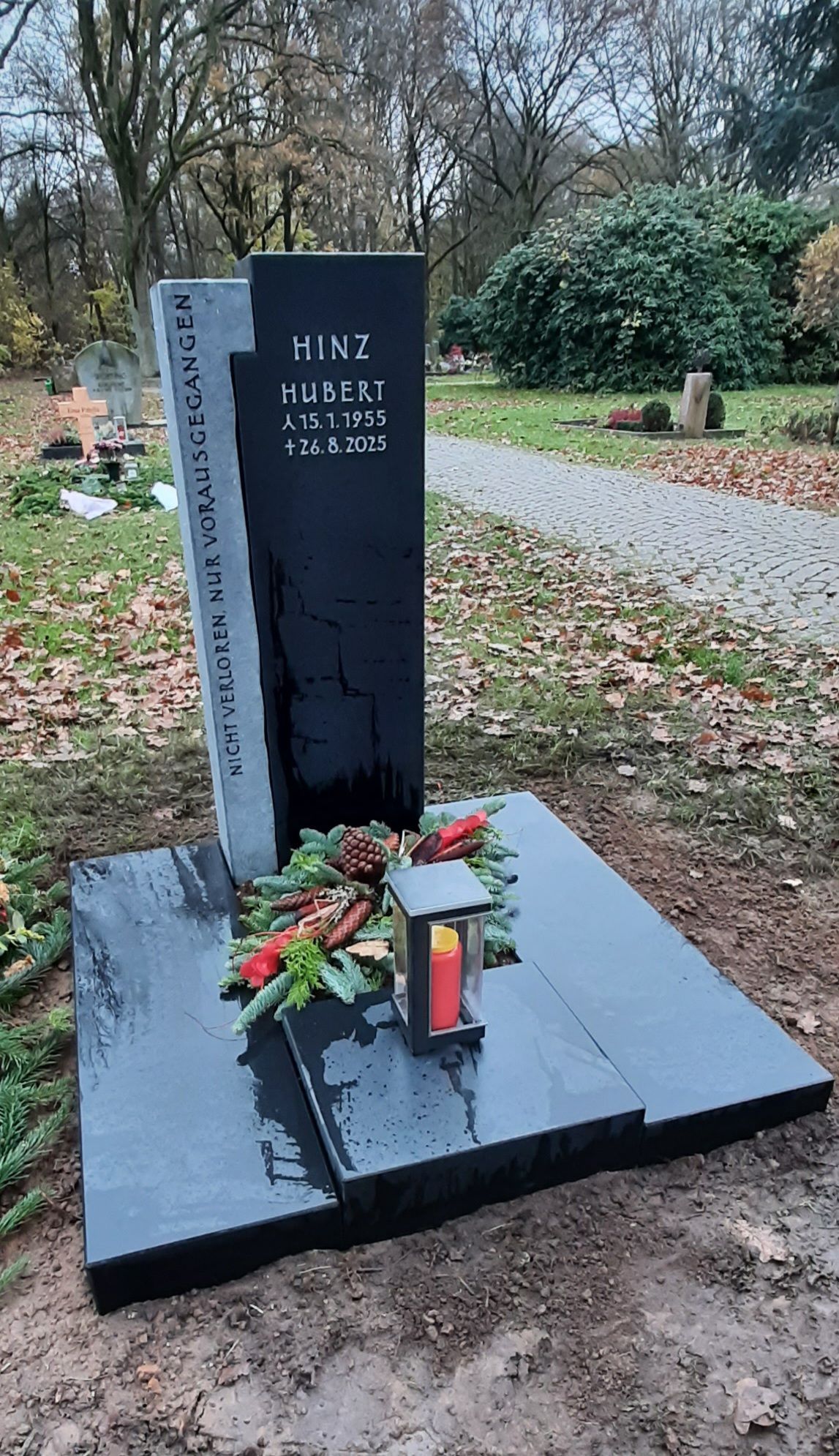 Schwarzes Gedenkmonument mit Blumen auf einem Steinsockel in einer bewaldeten Umgebung im Freien