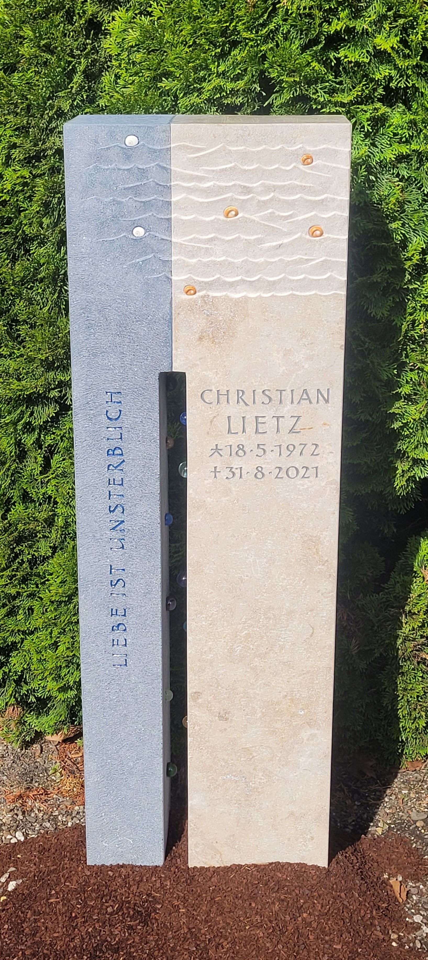 Zweigeteilter Stein mit Wellenstruktur und eingelassenen Glaselementen.