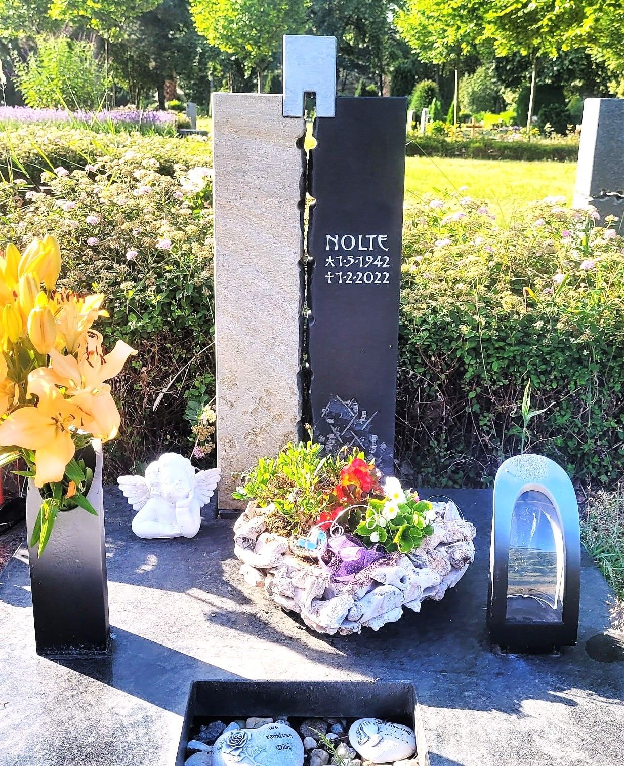 Zweiteiliges Grabmal aus hellem und dunklem Stein, verbunden durch ein Metallelement.