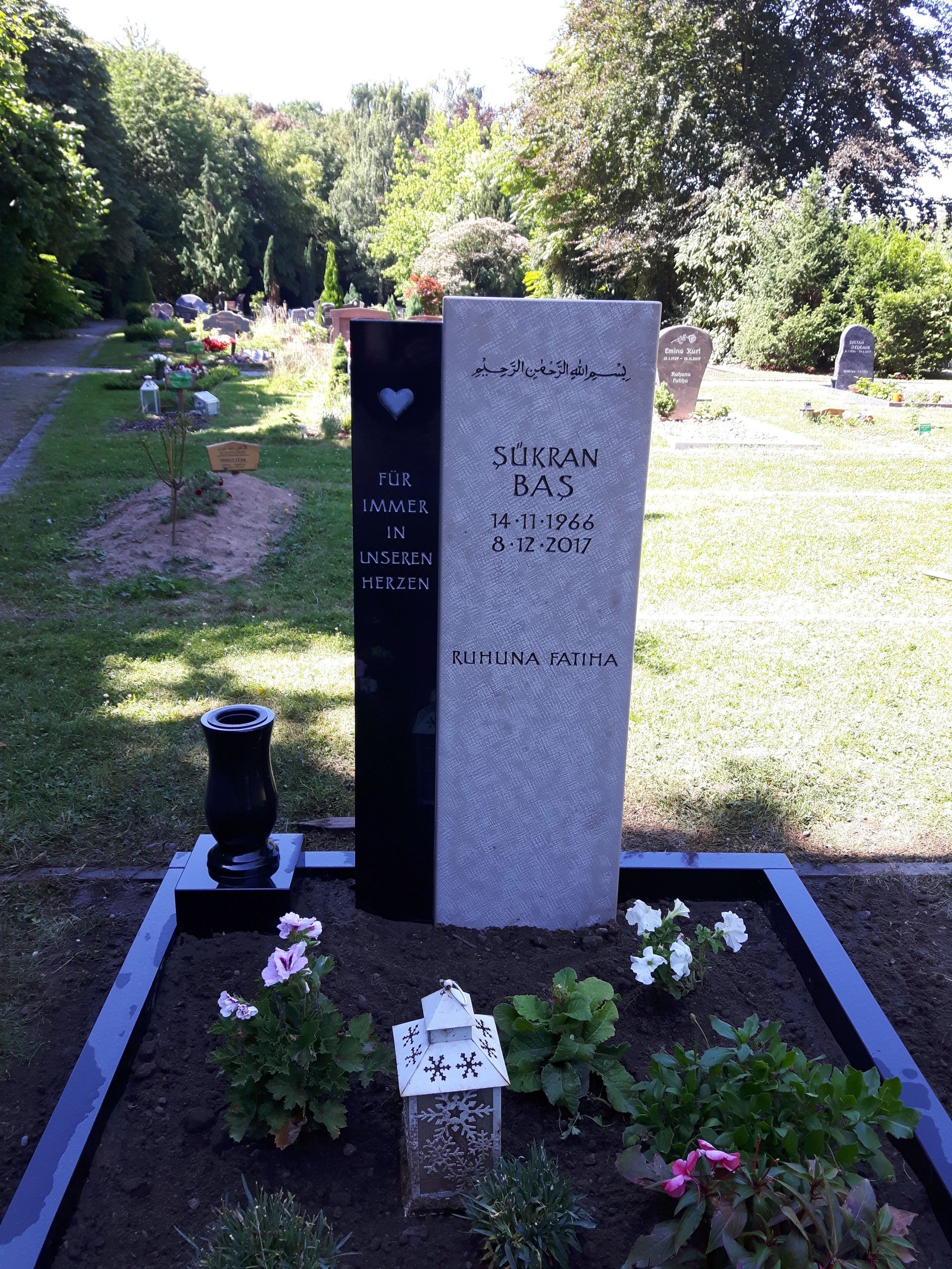Dunkles muslimisches Grabmal mit arabischer Schrift in einer Friedhofsanlage.