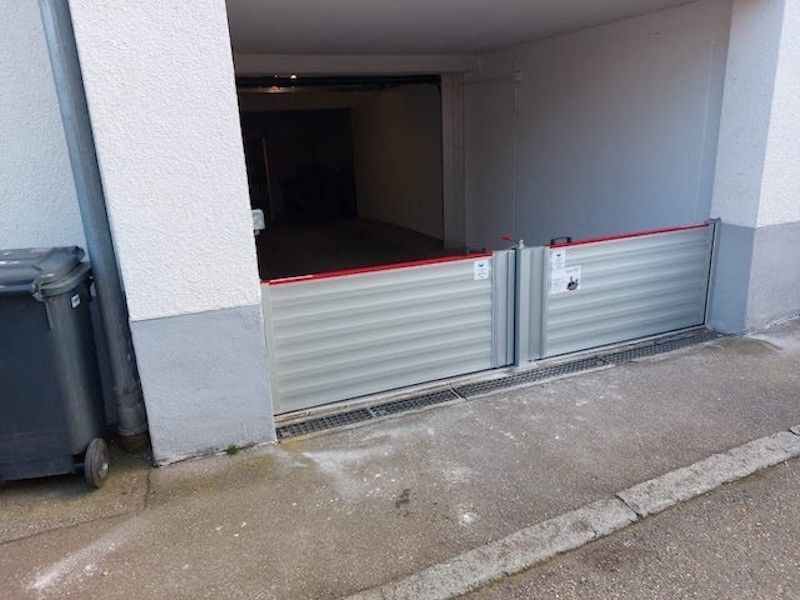 Hochwasserschutzbarriere an einer Garageneinfahrt installiert. Graue Metallpaneele, rote Oberseite, Betonboden.