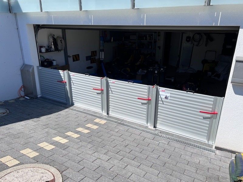 Hochwasserschutz vor einem Garagentor, graue Metallpaneele, rote Griffe, Terrasse.
