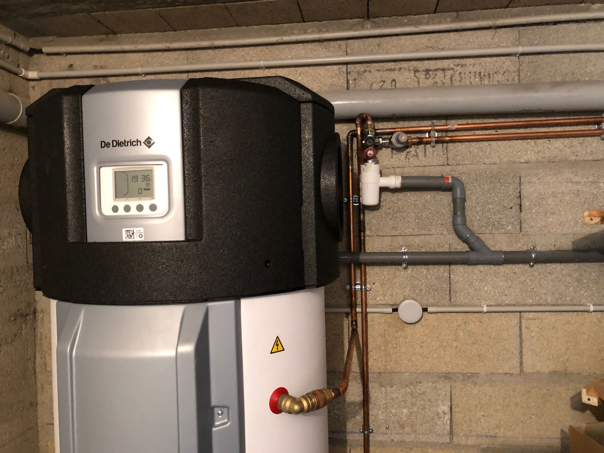 Un chauffe-eau avec panneau de commande, tuyaux et raccords dans un sous-sol.