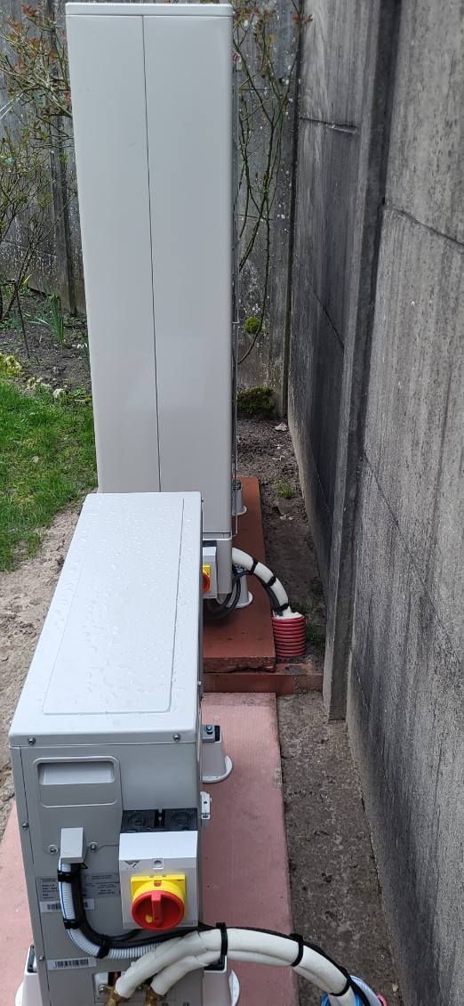 Équipement électrique extérieur, deux boîtiers blancs avec câblage, posés sur une surface rouge près d'un mur en béton.