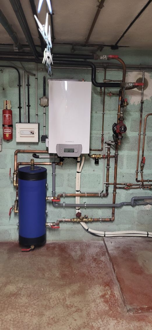 Un système de chauffe-eau dans une buanderie avec des tuyaux, un réservoir bleu et un extincteur sur le mur.