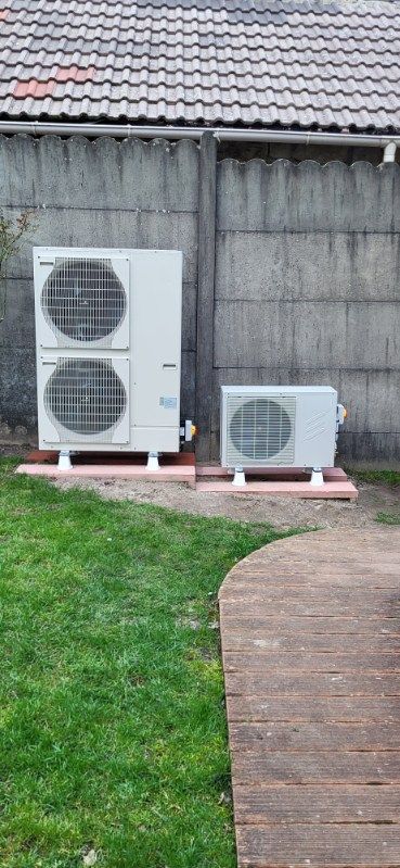 Deux unités de climatisation blanches à l'extérieur contre un mur gris avec de l'herbe et une passerelle.