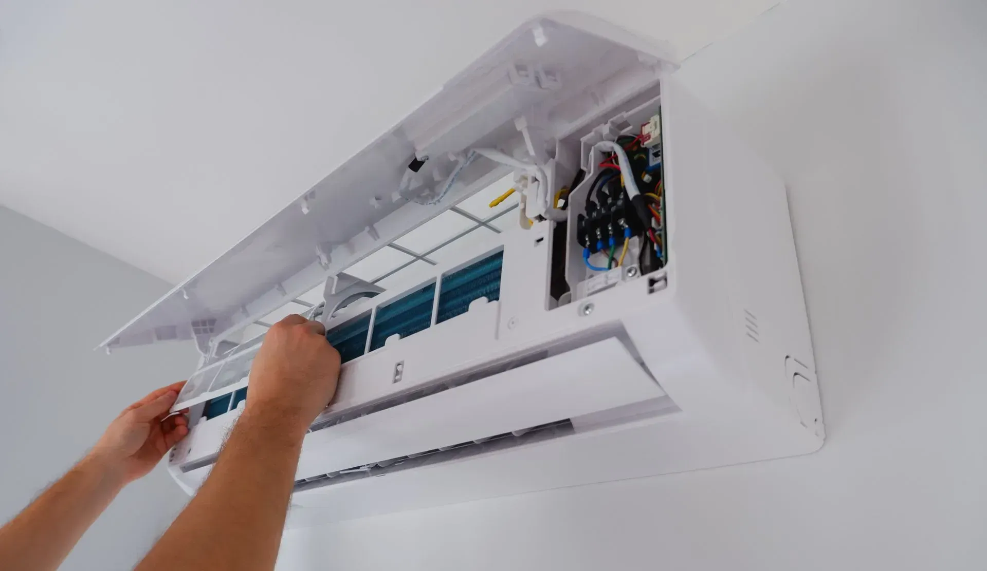 Mains retirant le filtre à air d'un climatiseur mural blanc.
