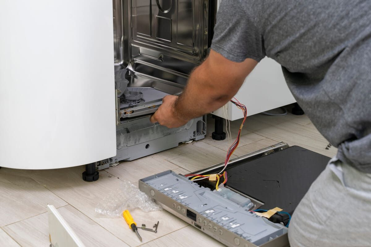 Técnico reparando el interior abierto de un electrodoméstico blanco con herramientas cerca