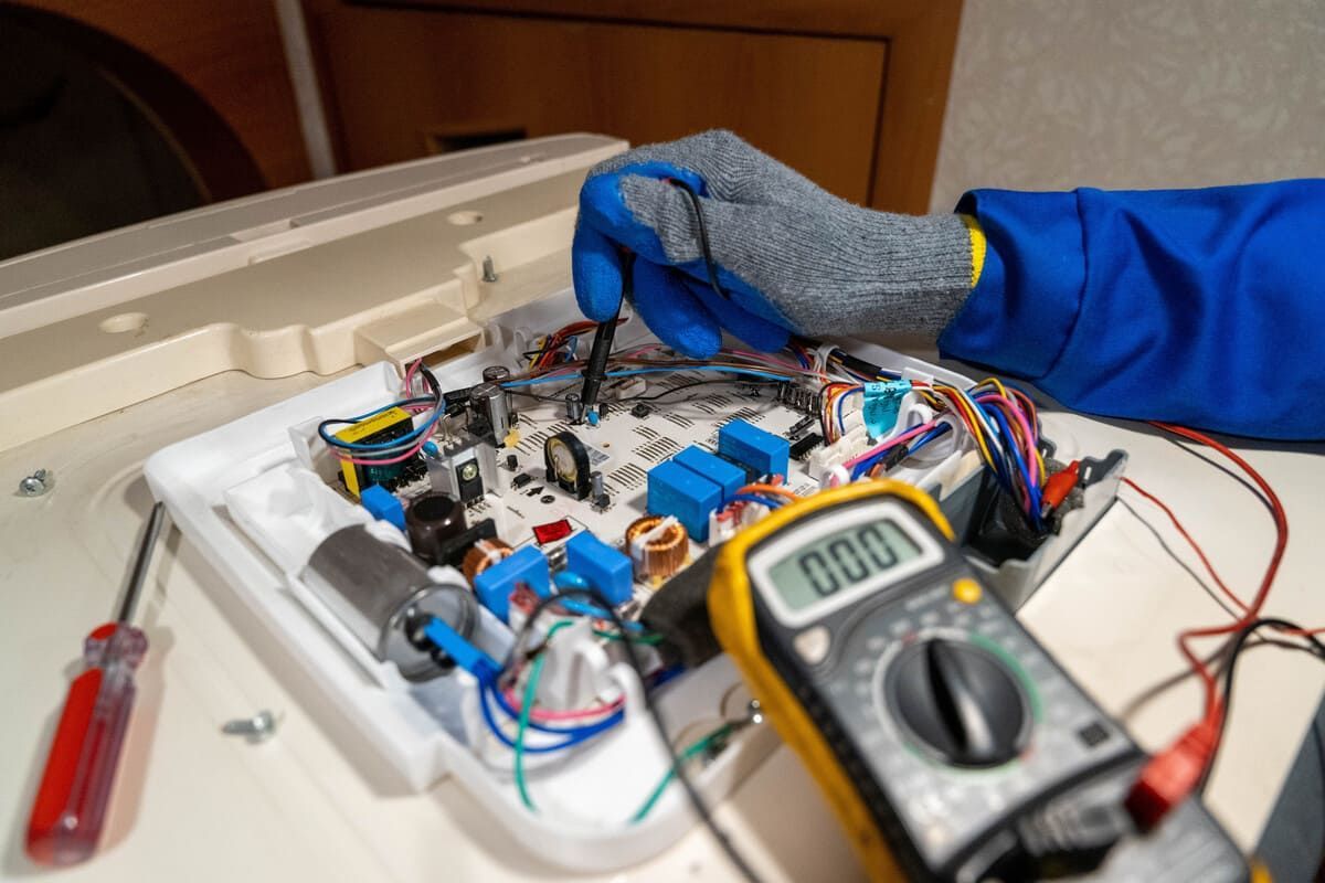 Una mano enguantada ajusta los cables de una pequeña placa de circuitos electrónicos, con un multímetro en primer plano.