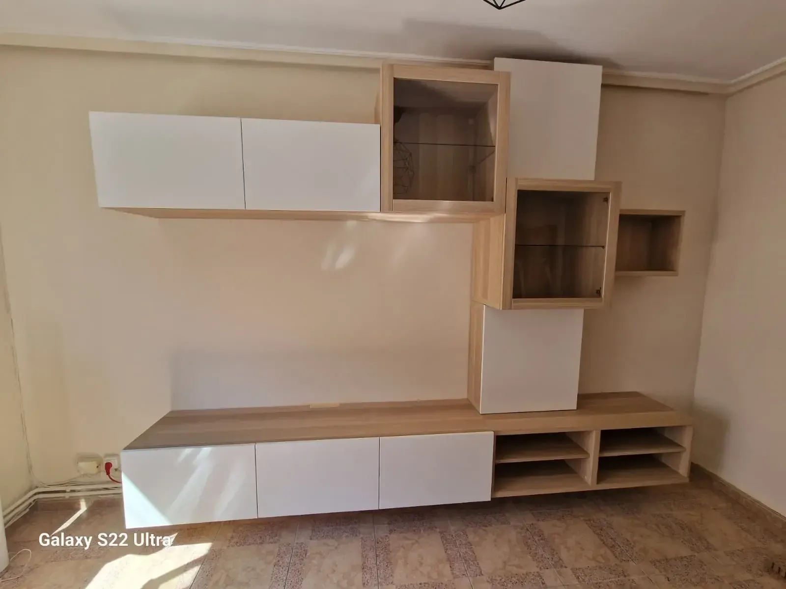 Mueble multimedia moderno de pared en color beige y blanco con estantes abiertos y armarios cerrados.