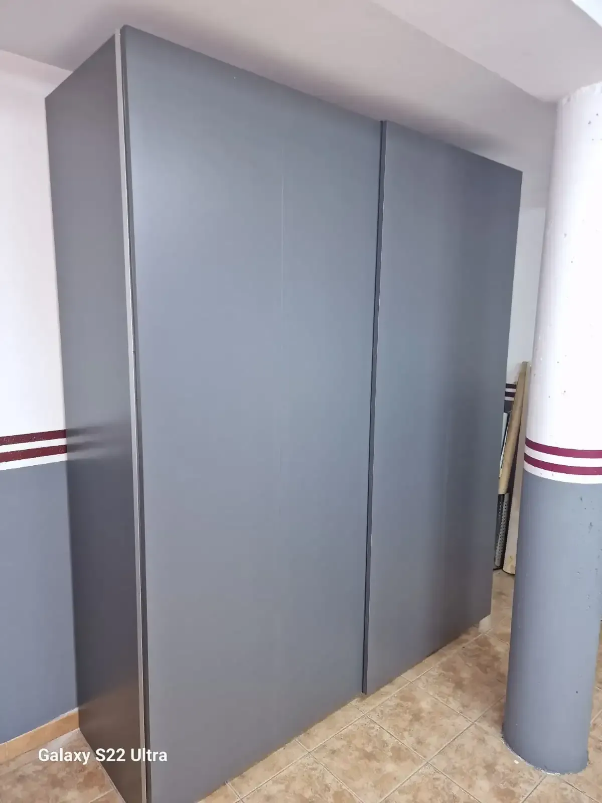 Armario gris con puertas correderas, contra una pared gris y blanca.