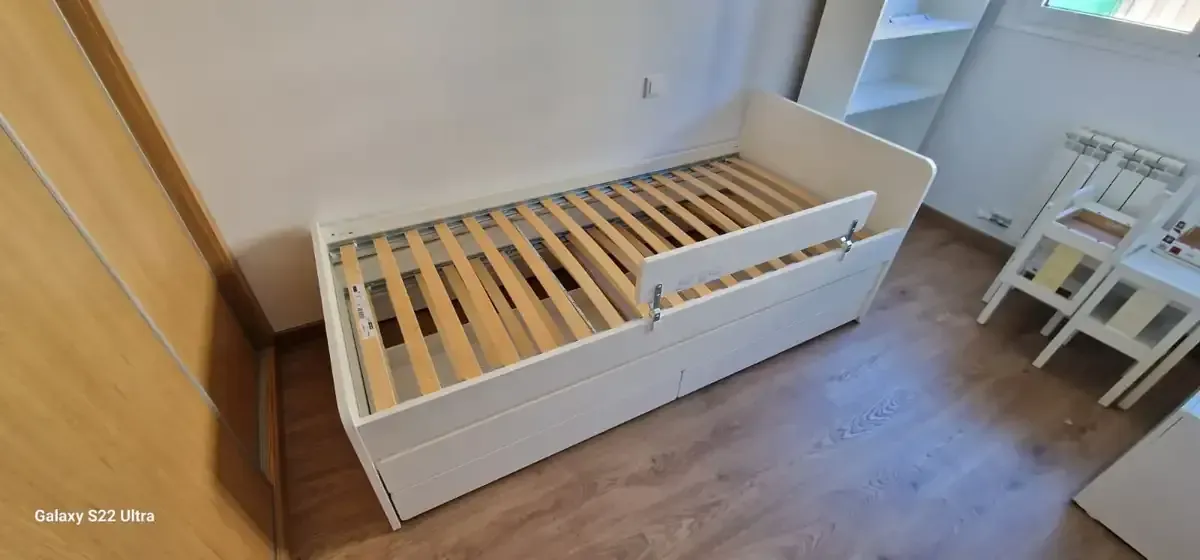 Estructura de cama blanca con láminas de madera, parcialmente extraíbles, en una habitación con suelo de madera clara.
