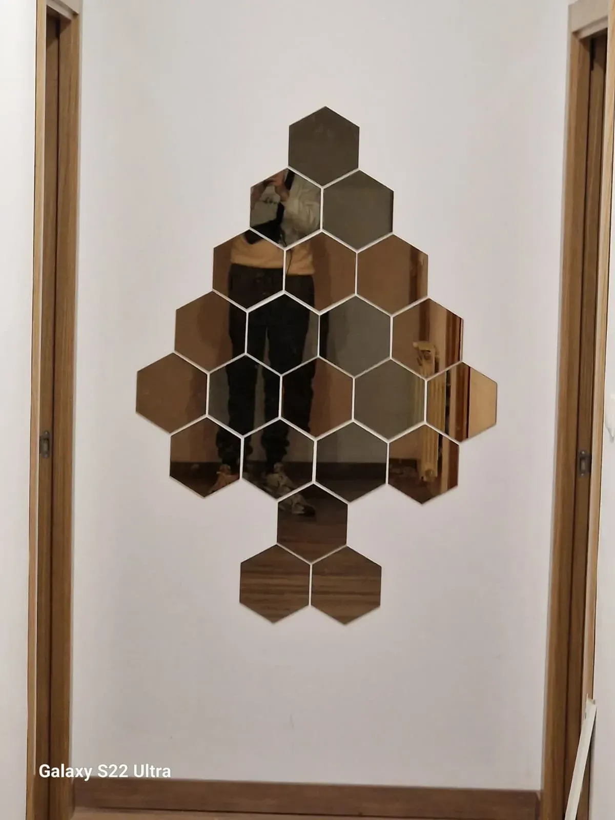 Espejos hexagonales dorados dispuestos en forma de pala sobre una pared blanca, enmarcados por molduras de madera.