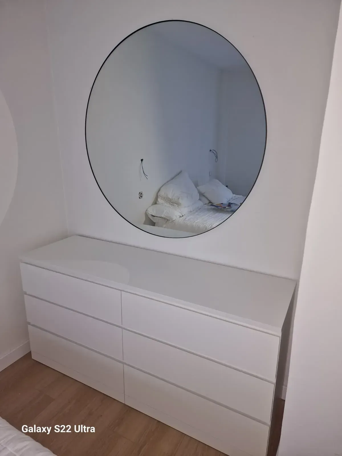Cómoda blanca con un gran espejo redondo colgado encima.