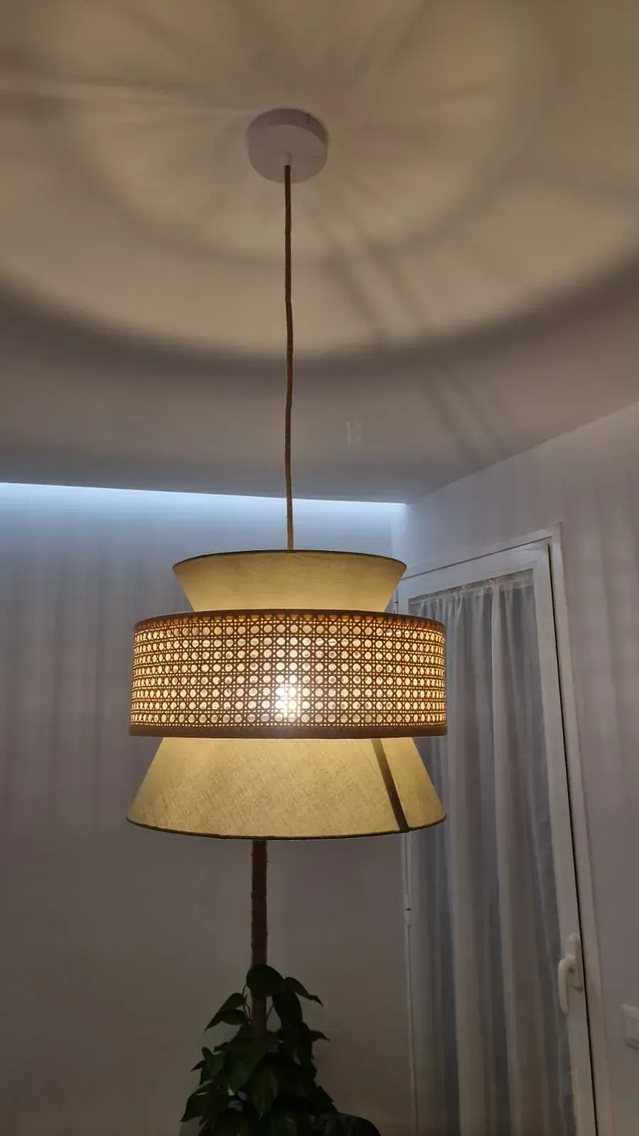 Lámpara colgante en capas con pantalla tejida natural, que proyecta luz sobre el techo, en una habitación.