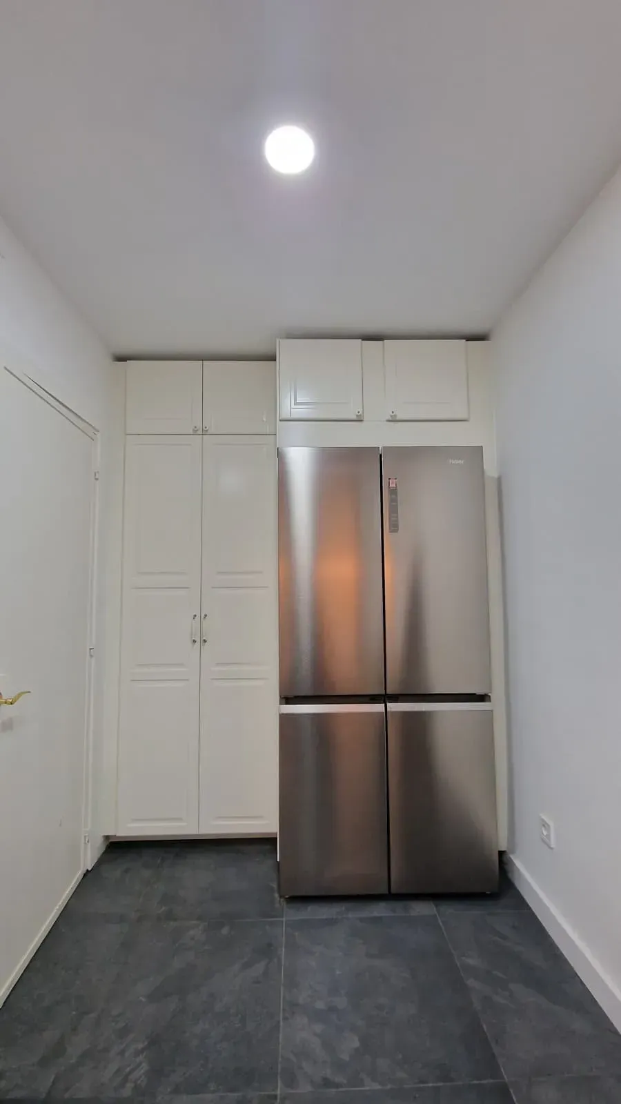 Cocina con refrigerador de acero inoxidable, gabinetes blancos y piso de baldosas oscuras.
