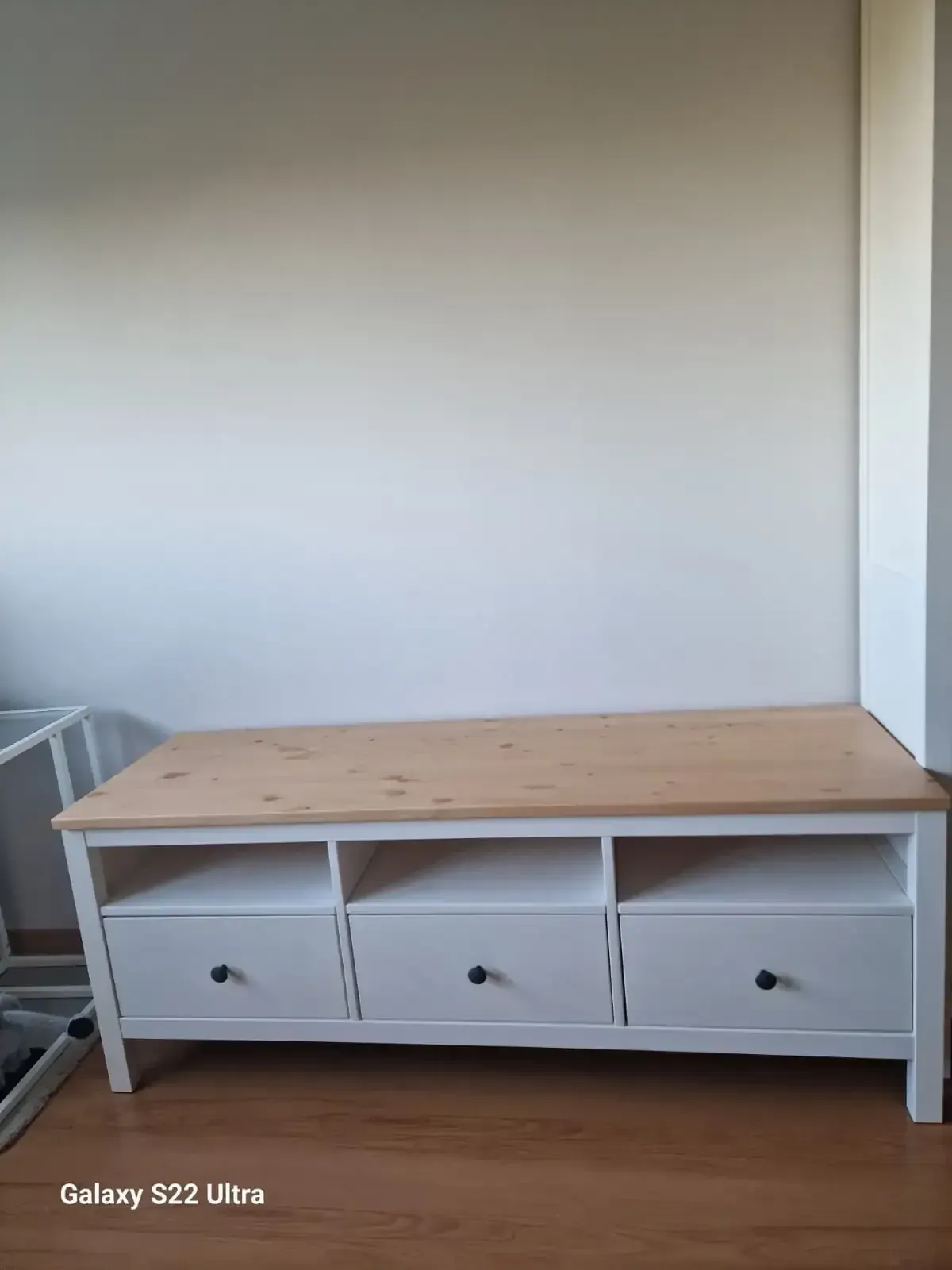 Mueble de TV de tres cajones en color blanco y madera contra una pared clara, en una habitación con suelo de madera.
