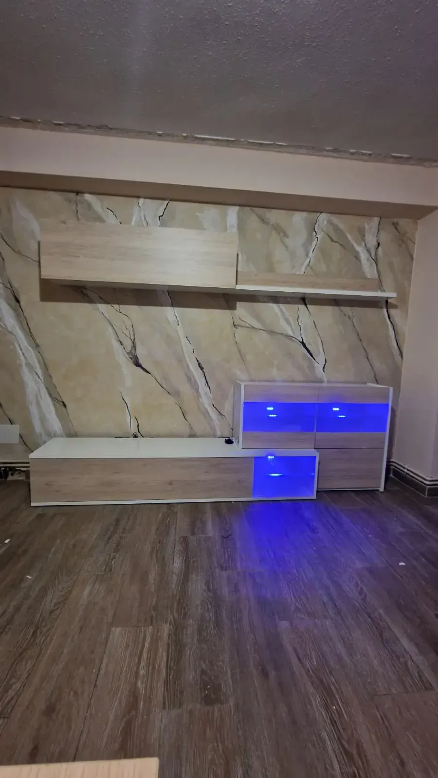 Centro de entretenimiento de madera con luces LED azules contra una pared con diseño de mármol.