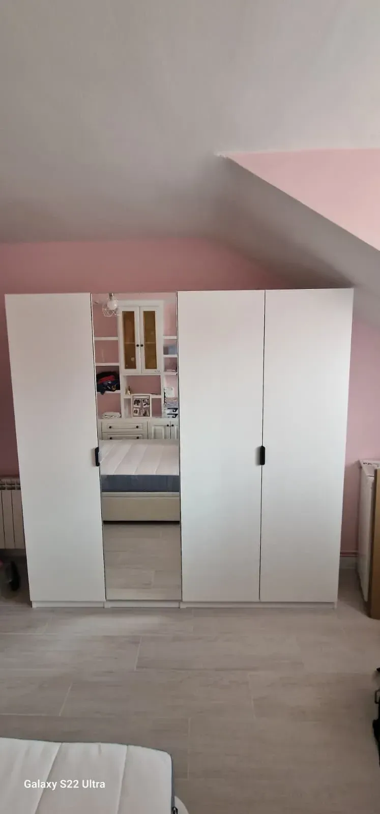 Armario blanco de cuatro puertas en una habitación con pared rosa y suelo de madera clara.