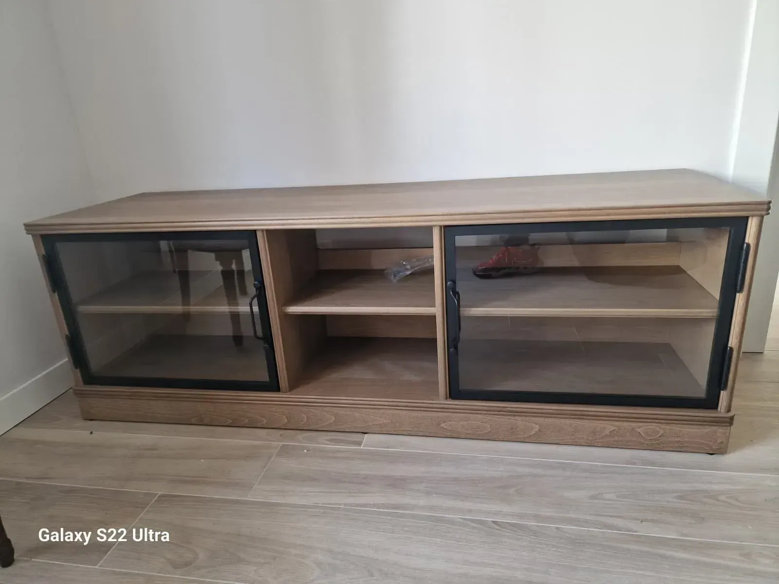 Mueble de TV de madera con puertas de cristal y estantes contra una pared blanca.