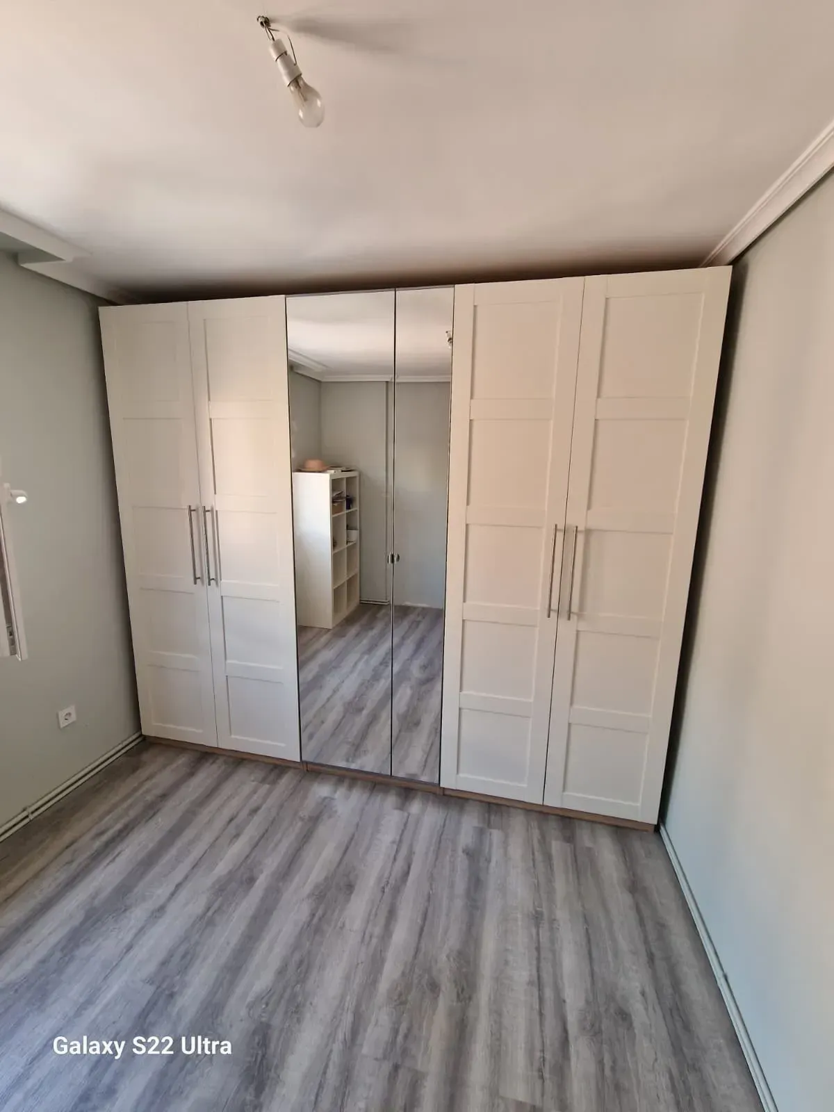 Armario blanco con sección central con espejo, piso gris y paredes neutrales.