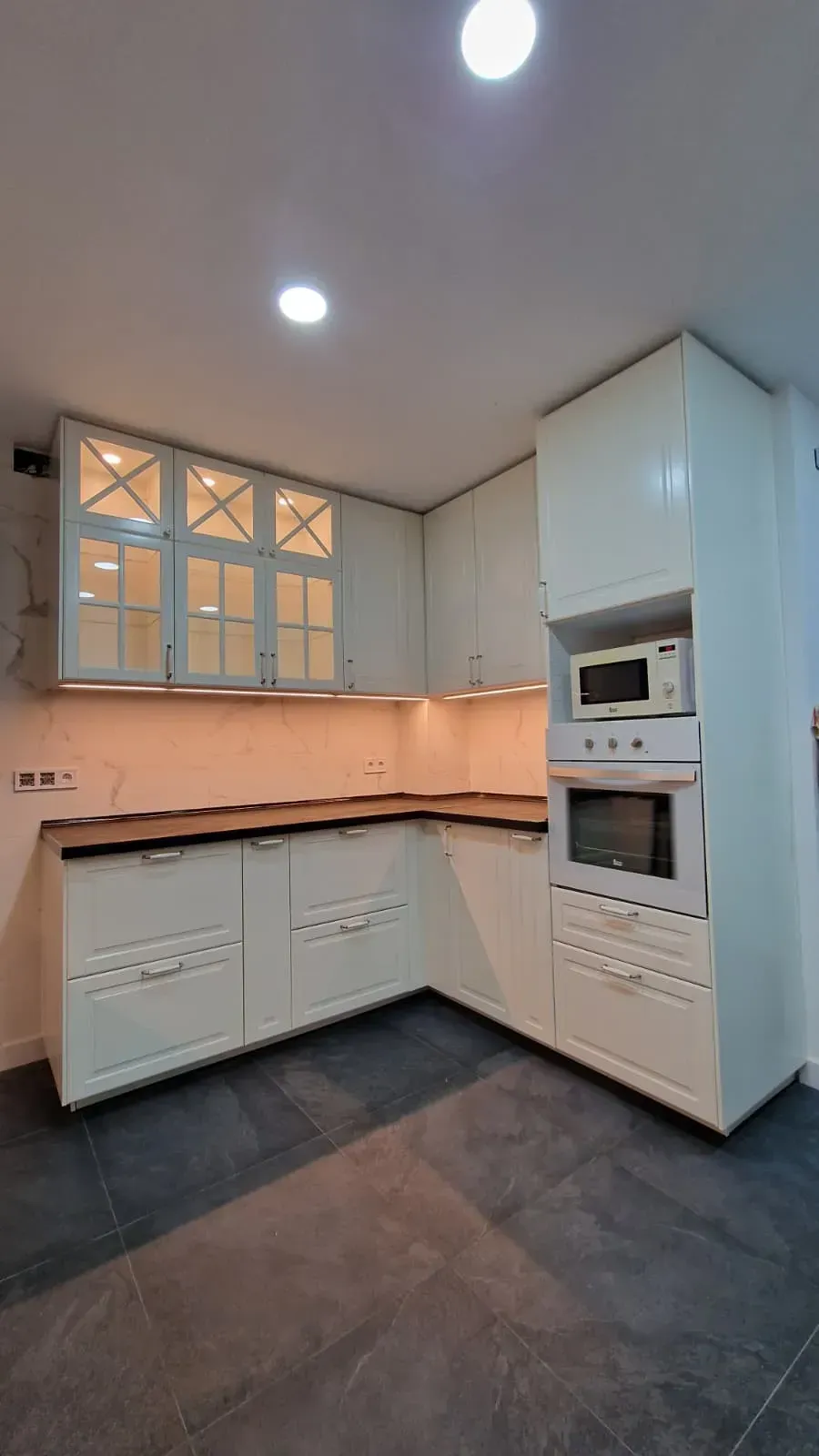 Muebles de cocina en color crema y encimera de madera en esquina, con microondas y horno integrados.