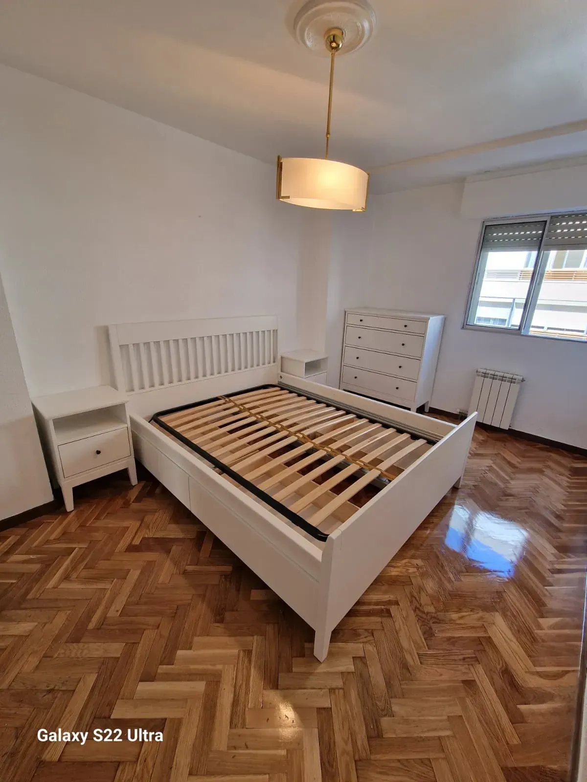 Juego de muebles de dormitorio en color blanco con piso de madera; incluye cama, mesitas de noche y tocador.