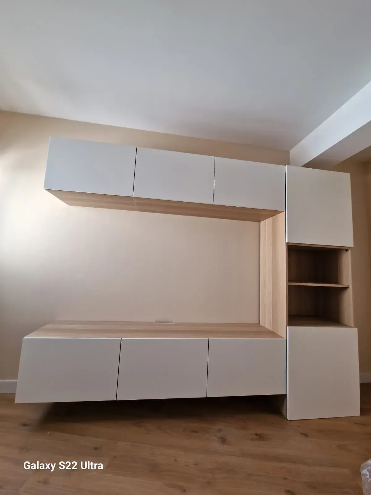 Mueble de almacenaje empotrado en blanco y madera, montado en la pared. Incluye armarios cerrados y estanterías abiertas.