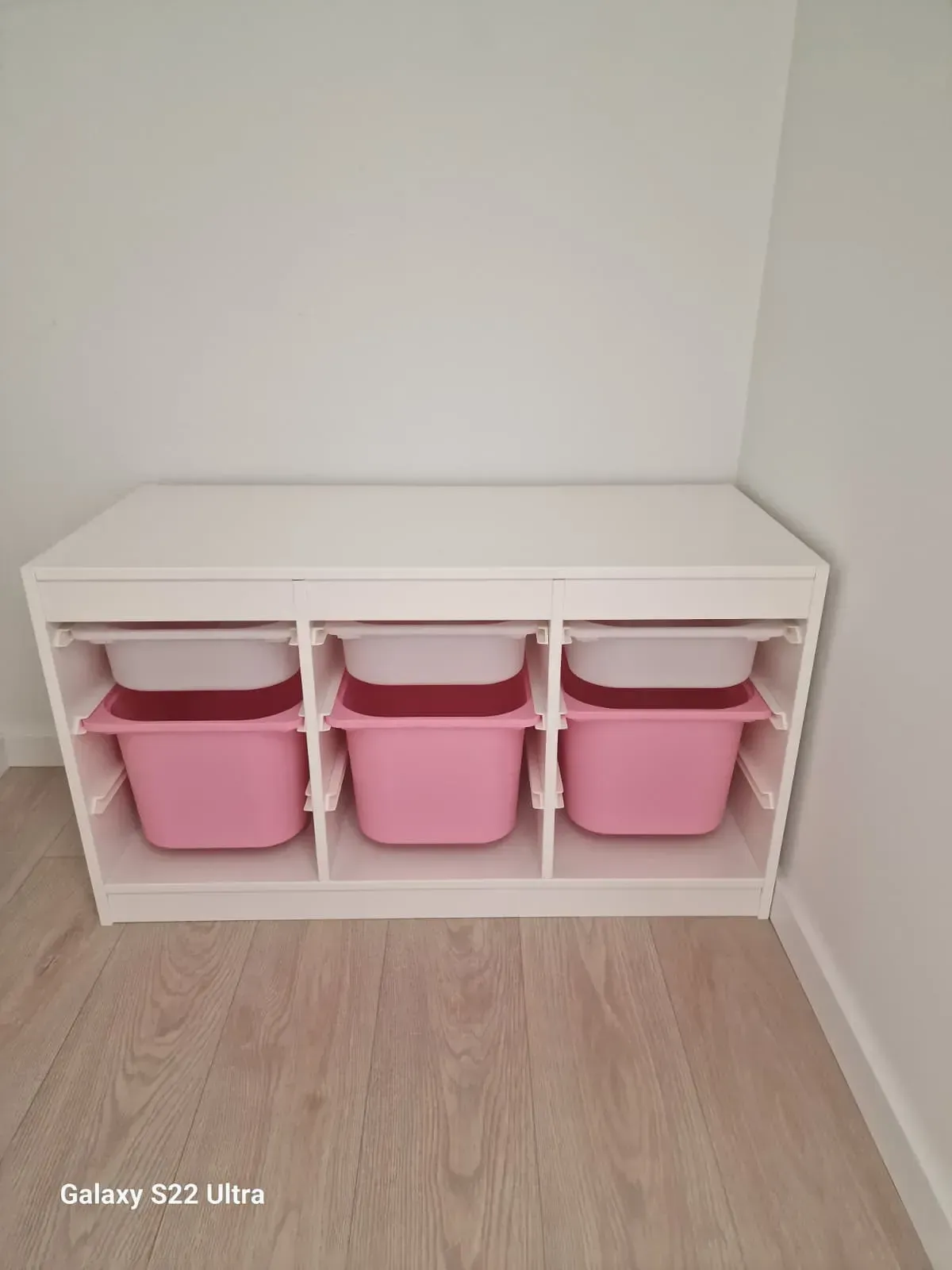 Unidad de almacenamiento blanca con tres contenedores rosas, contra una pared blanca.