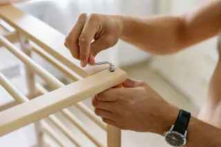 Persona ensamblando cuna de madera, fijando soporte de metal.