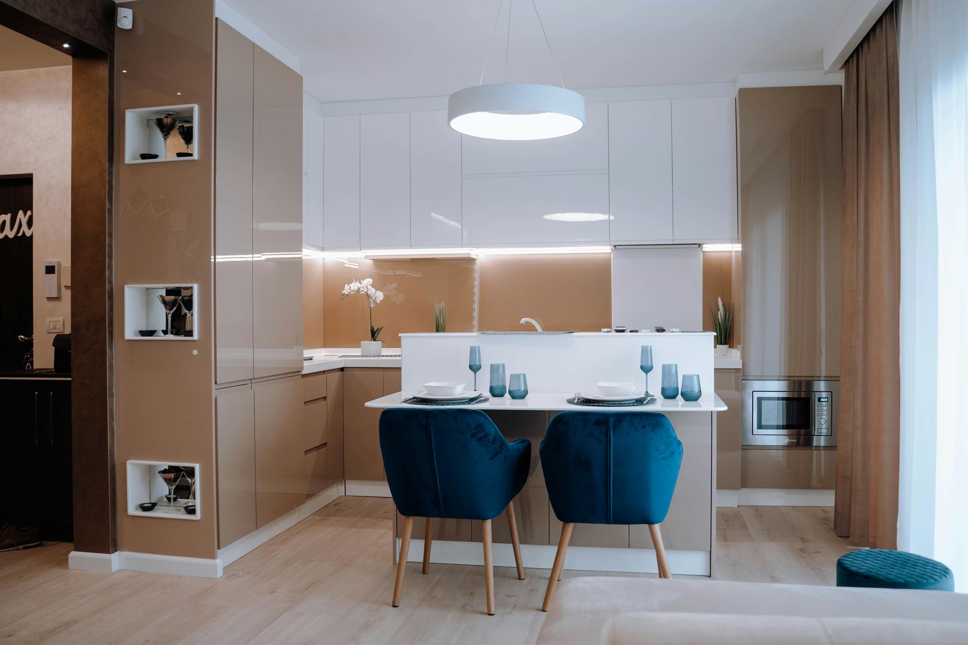 Cocina moderna con barra desayunadora y sillas azules; gabinetes beige, encimera blanca y microondas empotrado.