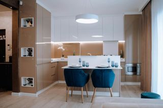 Cocina moderna con barra desayunadora y sillas azules; gabinetes beige, encimera blanca y microondas empotrado.