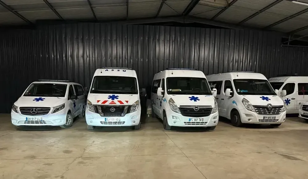 Quatre ambulances blanches garées côte à côte dans un garage, avec des marquages d’urgence bleus et rouges.