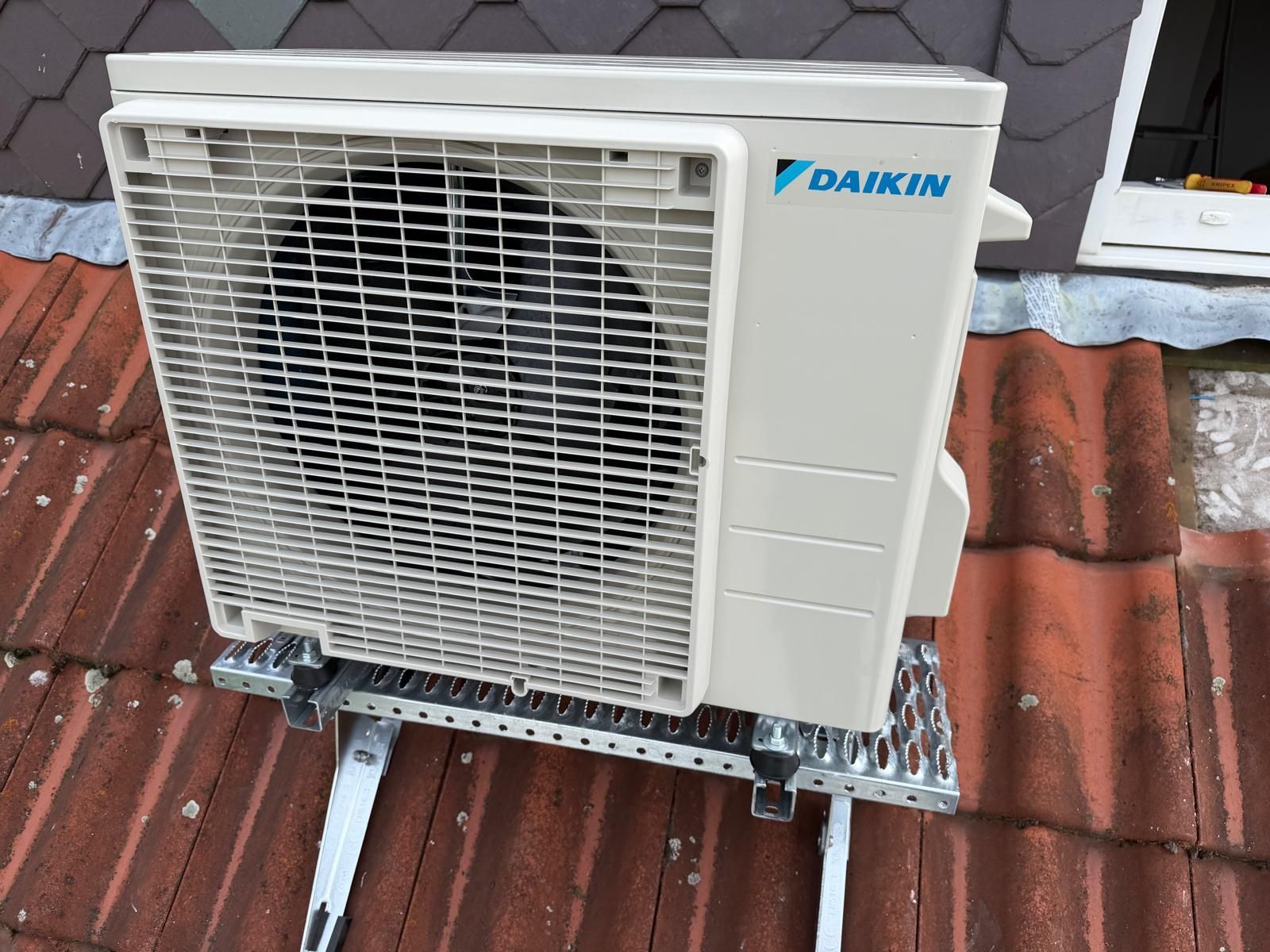 Daikin-Außengerät einer Klimaanlage, montiert auf einem Ziegeldach an einer Hauswand