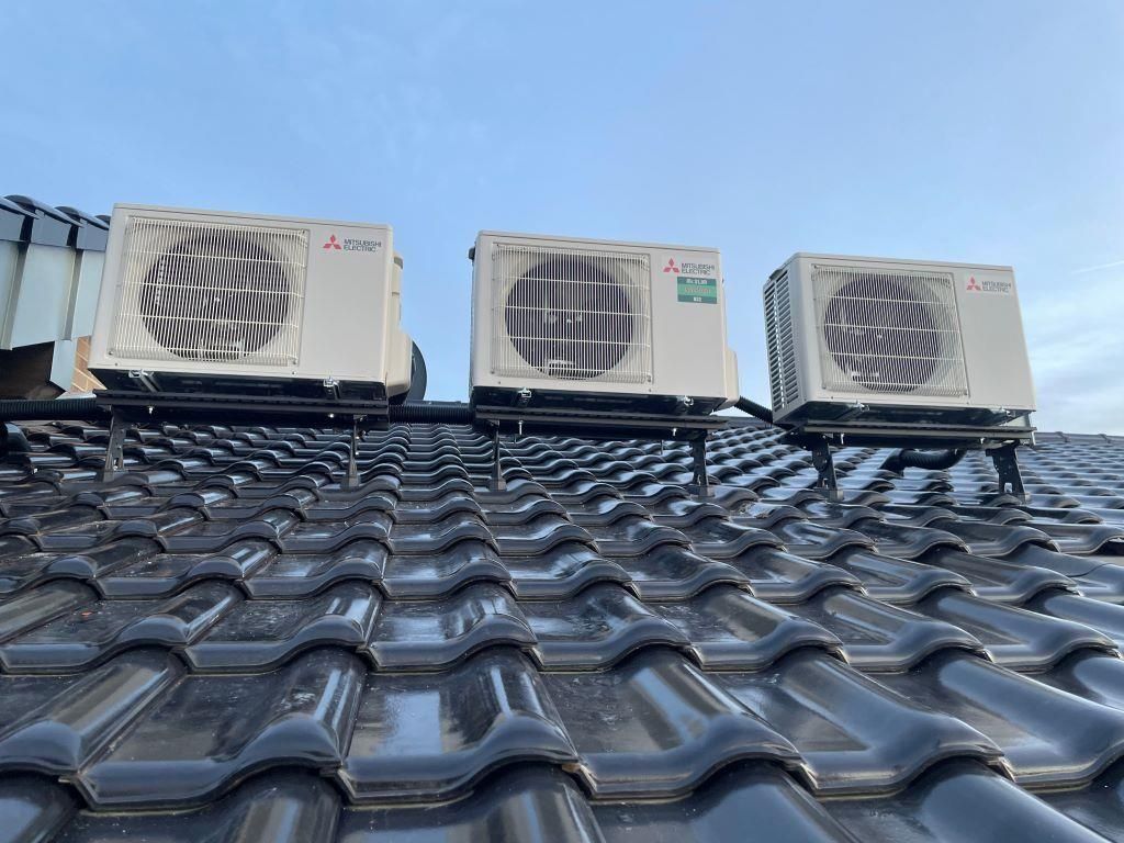 Auf einem Ziegeldach stehen drei Klimaanlagen.