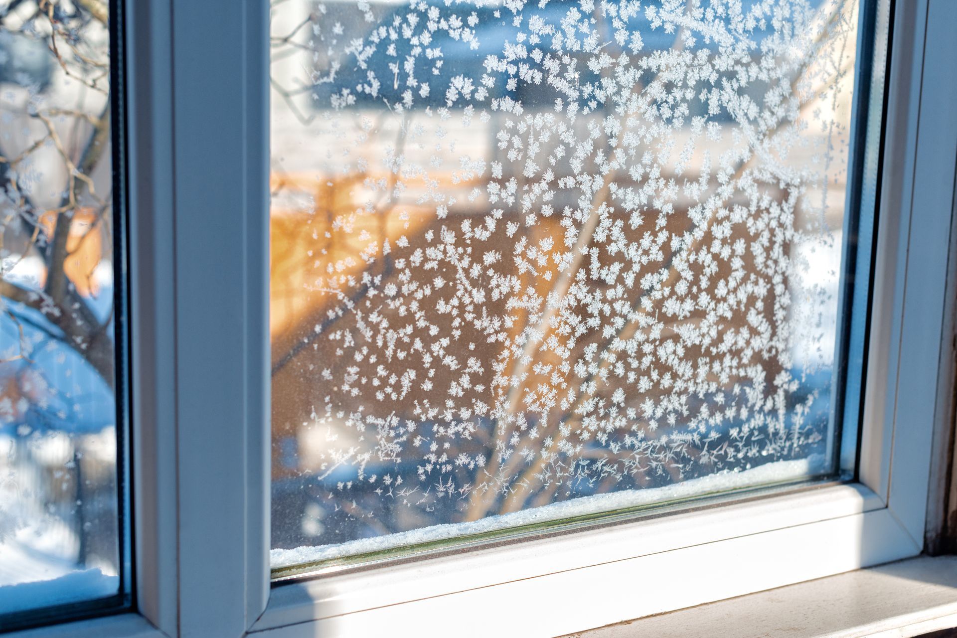 Schneeflocken auf einer Fensterscheibe, draussen ein verschwommener Sonnenuntergang.