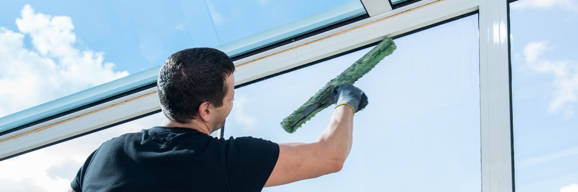 Eine Person mit blauen Handschuhen putzt ein Fenster mit einem Abzieher.