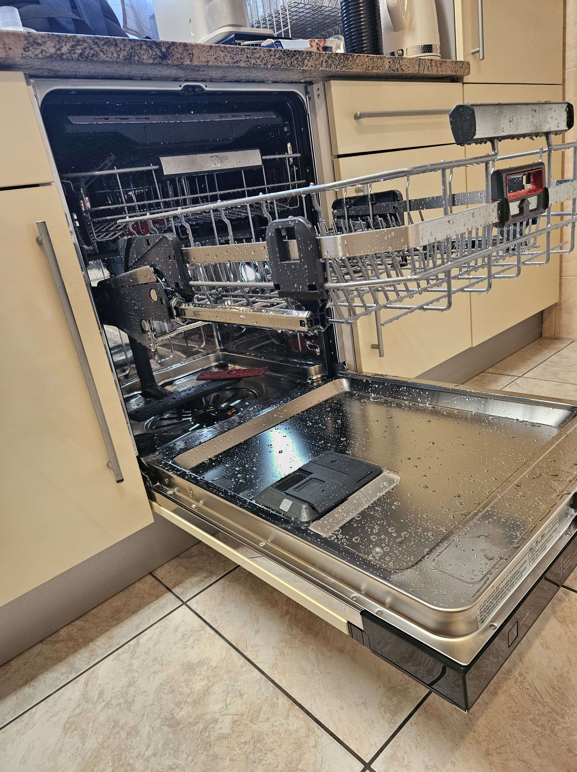 Lave-vaisselle porte ouverte, laissant apparaître les paniers, les buses et l'intérieur. Meubles beiges dans une cuisine.