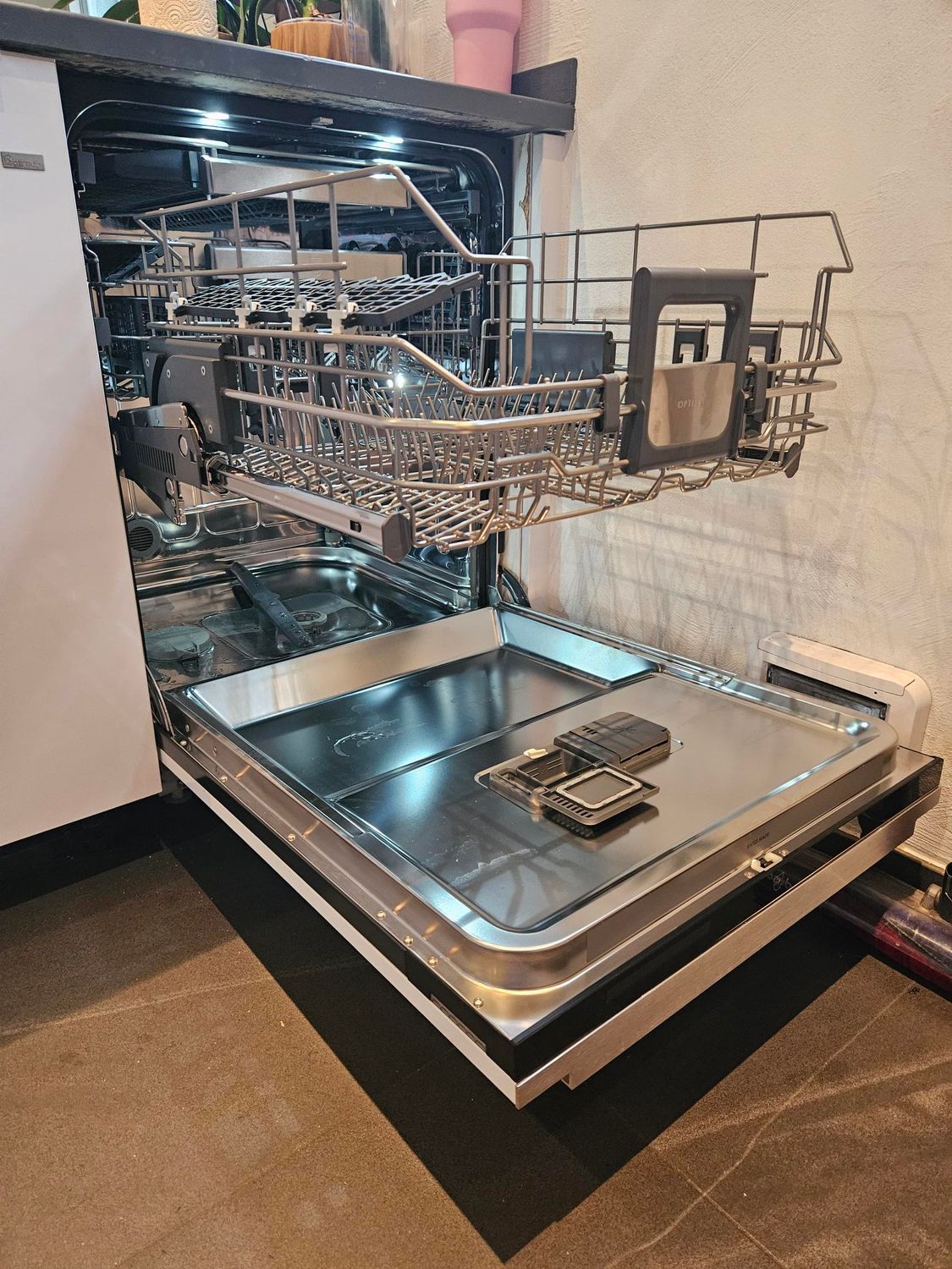 Lave-vaisselle ouvert, panier supérieur et tiroir à ustensiles tirés, intérieur éclairé.